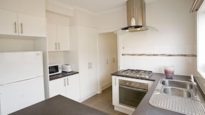 A compact kitchen with white cabinets, a microwave, a gas stove, and a sink. - City Condo (GOWANBRAE)