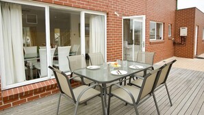A patio with a glass table and chairs, a brick wall, and a sliding glass door. - City Condo (GOWANBRAE)