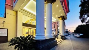 A hotel entrance with large columns, a statue, and a parking area. - Vienna Hotel (Shanghai)