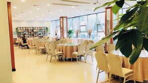 A spacious dining area with round tables and chairs, large windows, and a bookshelf in the background. - Vienna Hotel (Shanghai)
