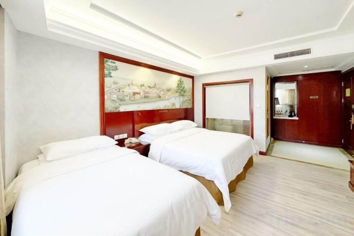 A hotel room with two beds, a painting on the wall, and a door leading to a bathroom.