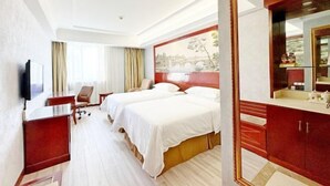 A hotel room with two beds, a desk, a chair, a TV, a large mirror, and a painting on the wall. - Vienna Hotel (Shanghai)