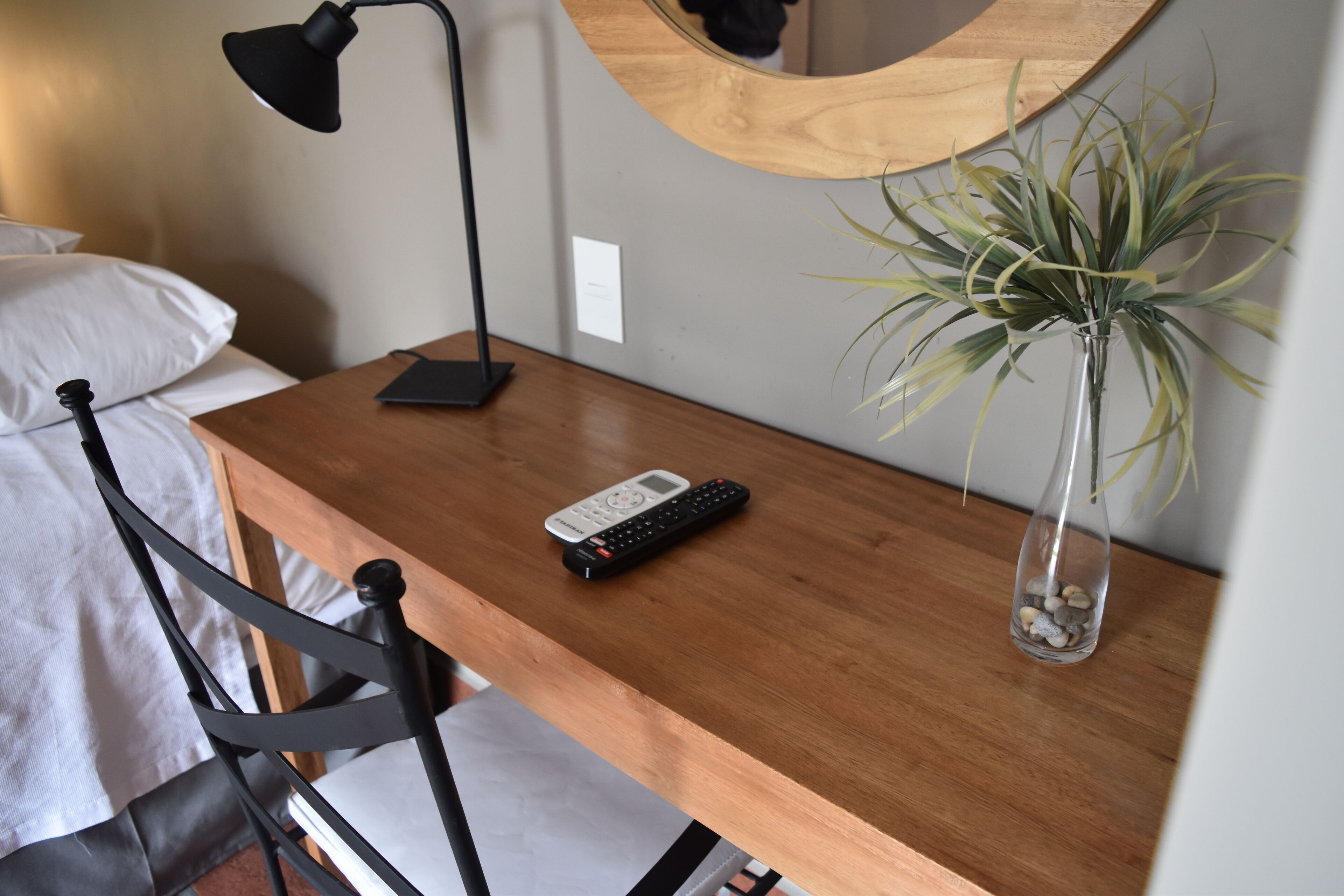 Un bureau en bois avec une télécommande, une lampe et un vase contenant une plante.