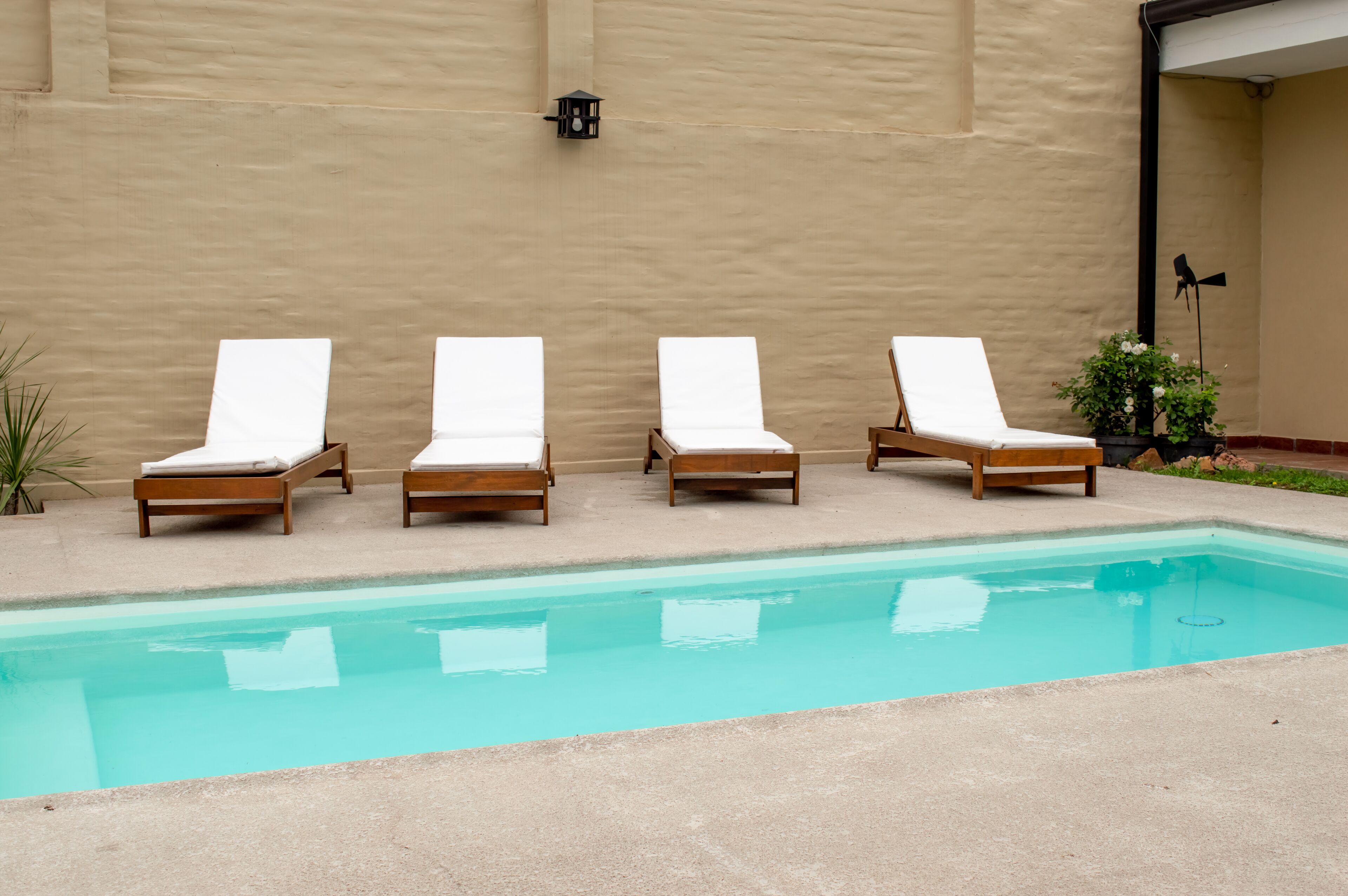 A pool area with four wooden lounge chairs and a light fixture on the wall.