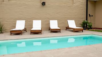 A pool area with four wooden lounge chairs and a light fixture on the wall.