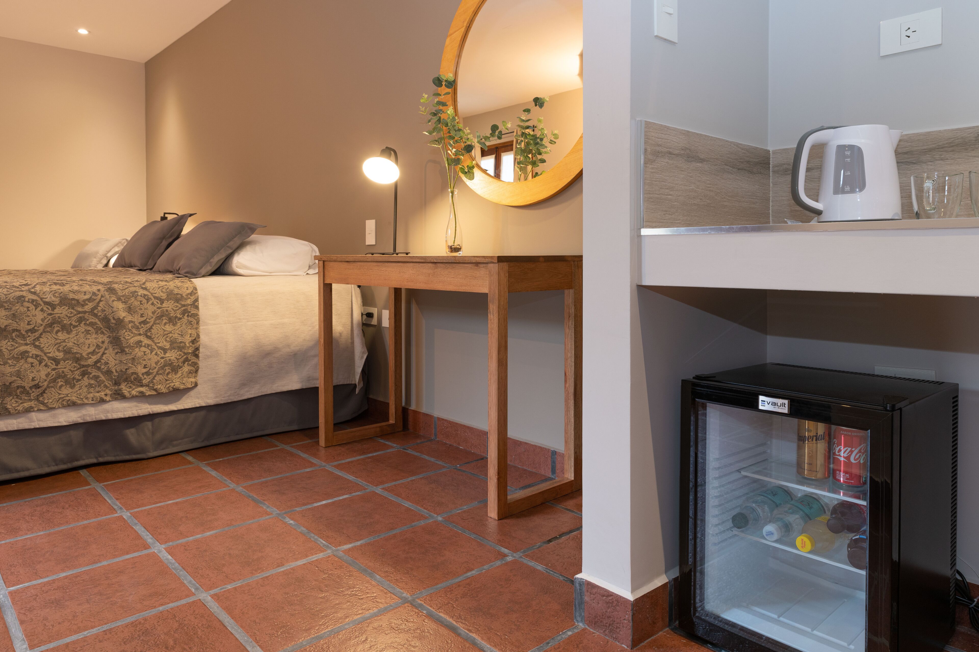 A bedroom with a bed, bedside table, mirror, and a minibar.