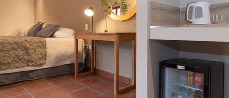 A bedroom with a bed, bedside table, mirror, and a minibar.