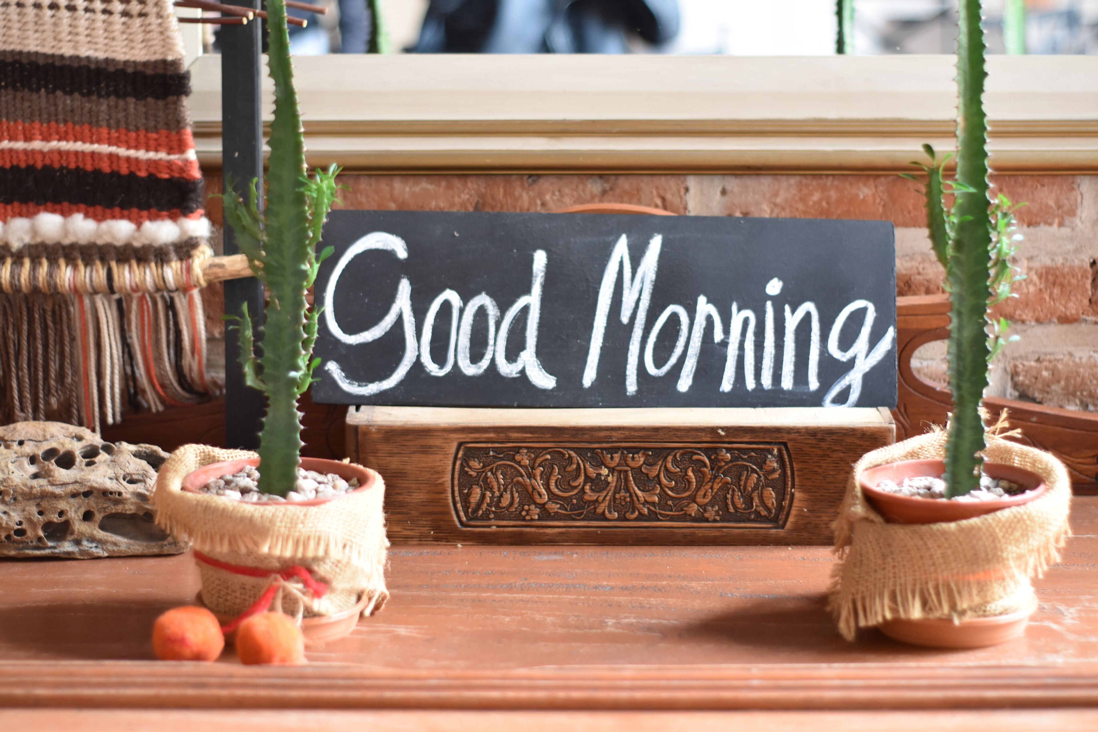 Un interno rustico con un cartello che riporta 'Good Morning', due cactus in vaso e un cesto di vimini.