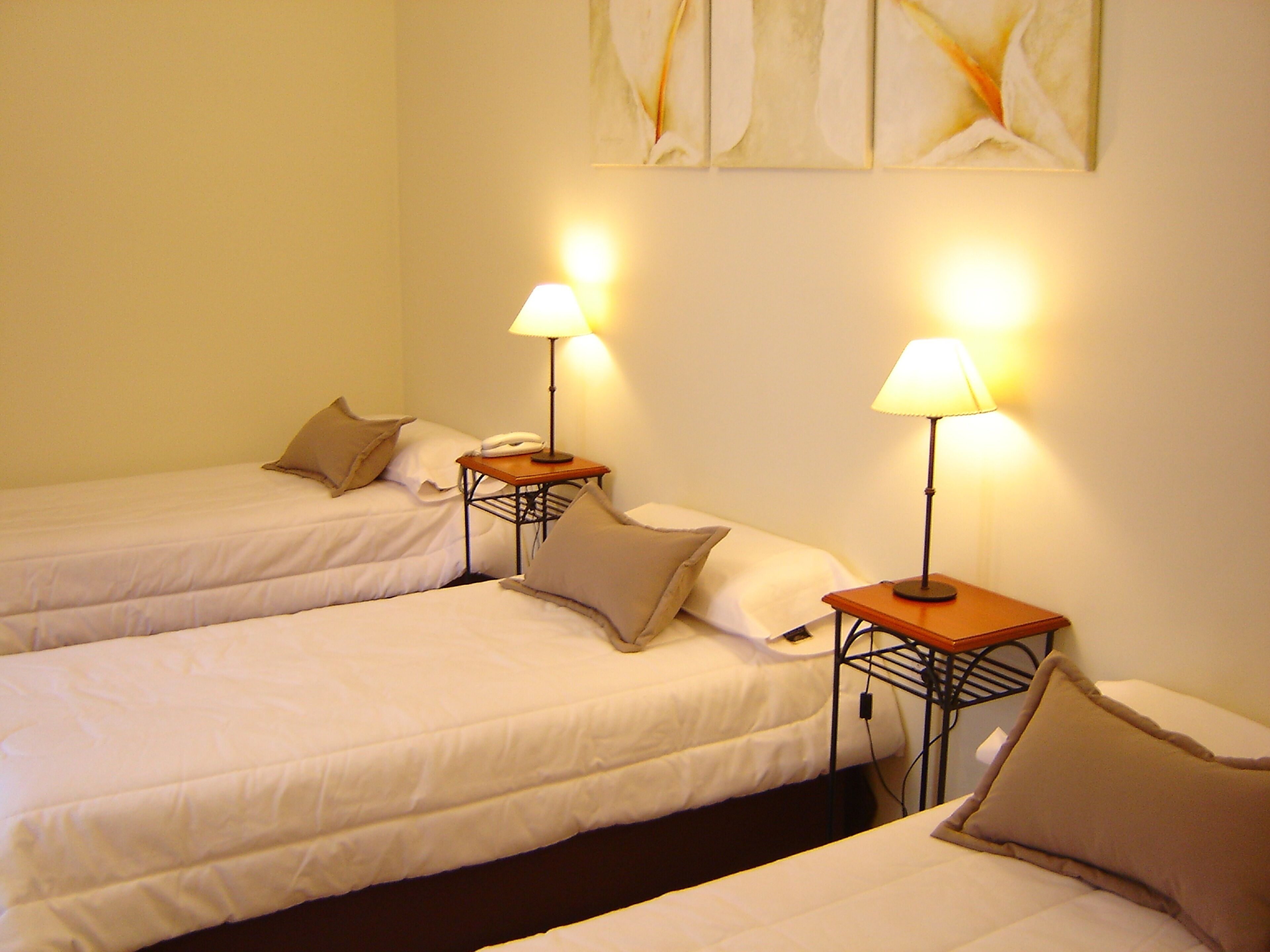Habitación de hotel con dos camas individuales, cada una con mesita de noche, lámpara y teléfono.
