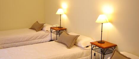 Habitación de hotel con dos camas individuales, cada una con mesita de noche, lámpara y teléfono.
