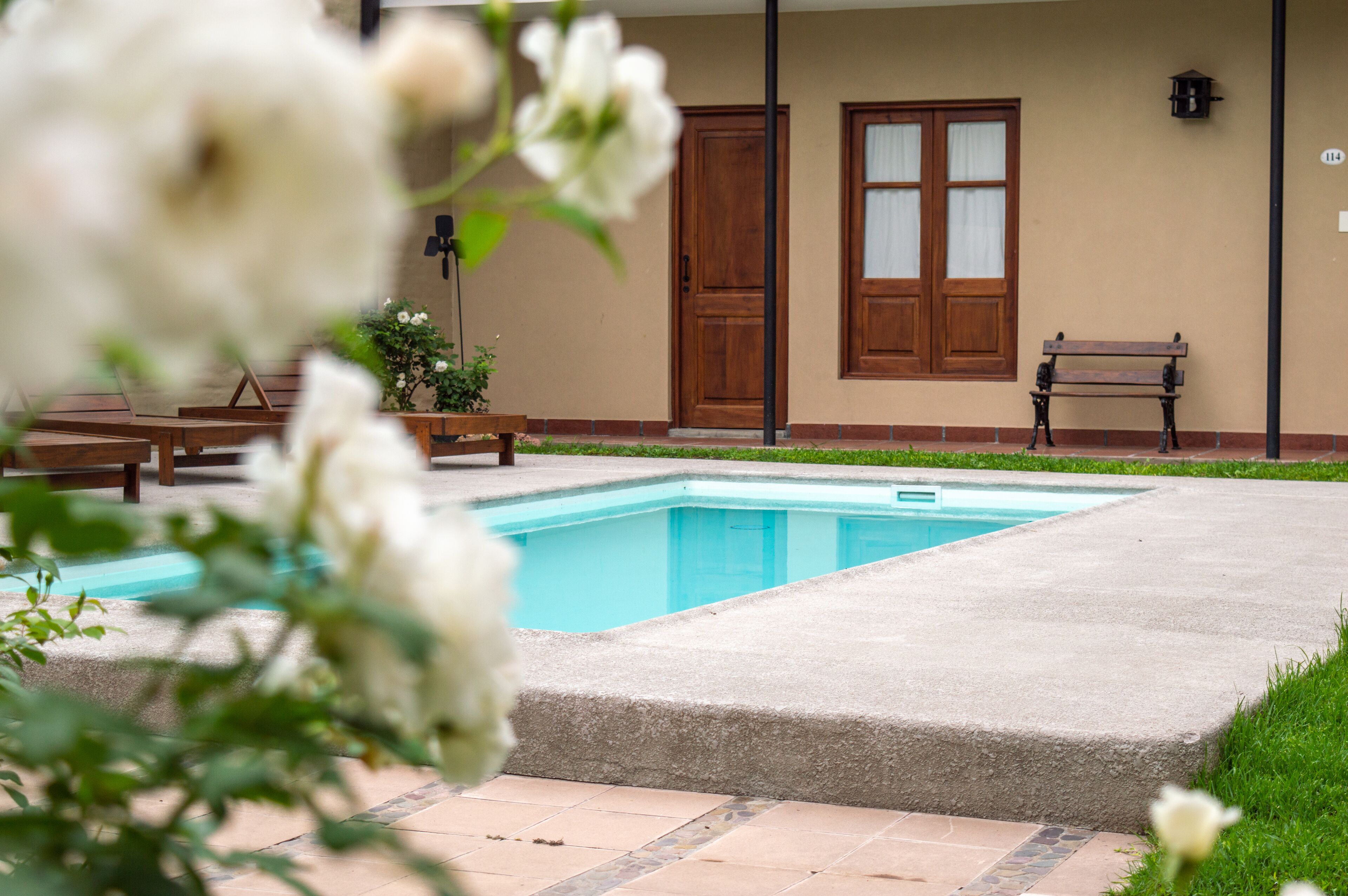 A swimming pool with a wooden deck, a bench, and a door in the background.
