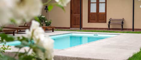 A swimming pool with a wooden deck, a bench, and a door in the background.