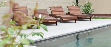 A poolside area with wooden lounge chairs and a small potted plant.