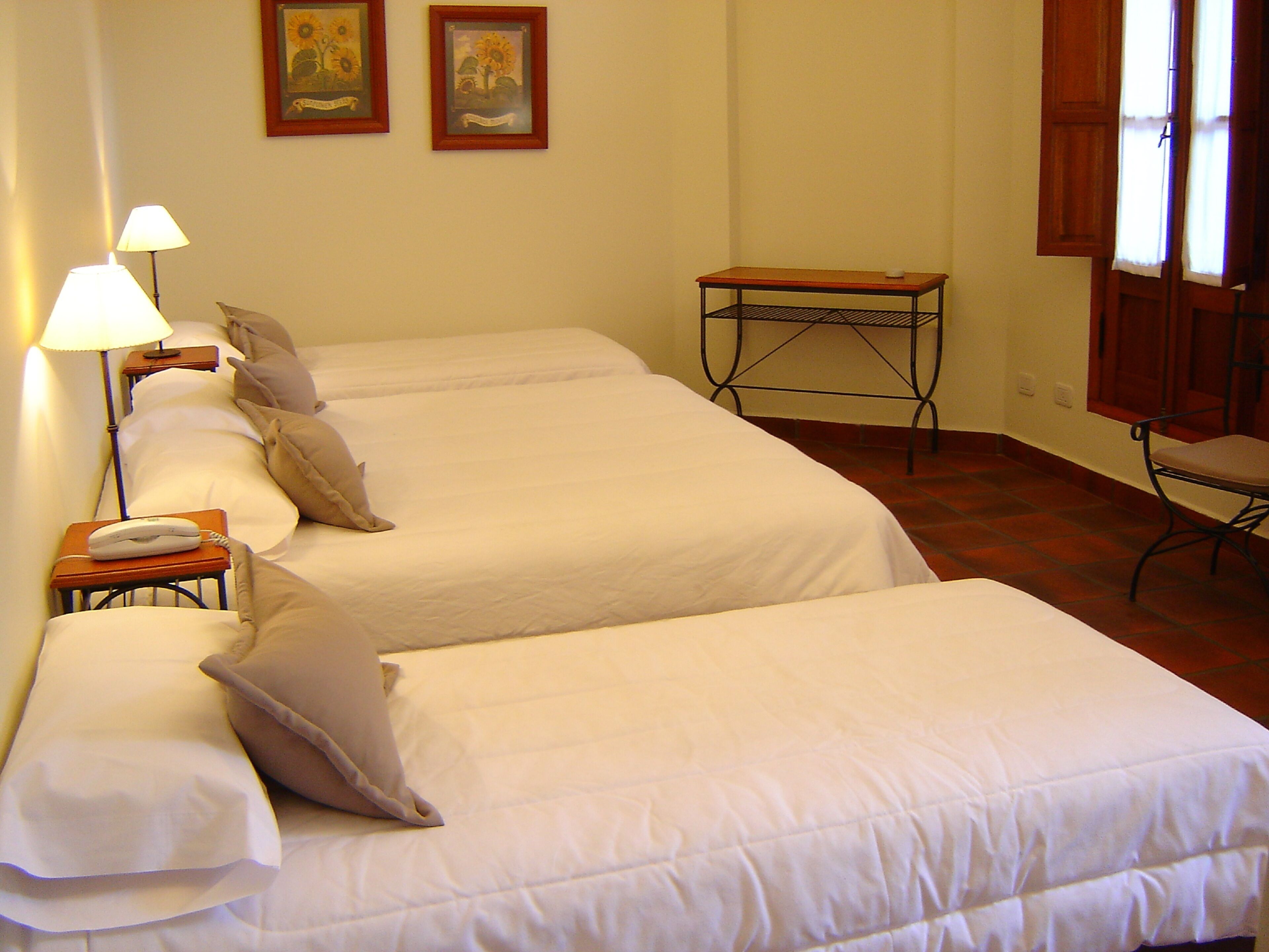 A hotel room with two beds, a bedside table with a lamp, a small table, and a chair.