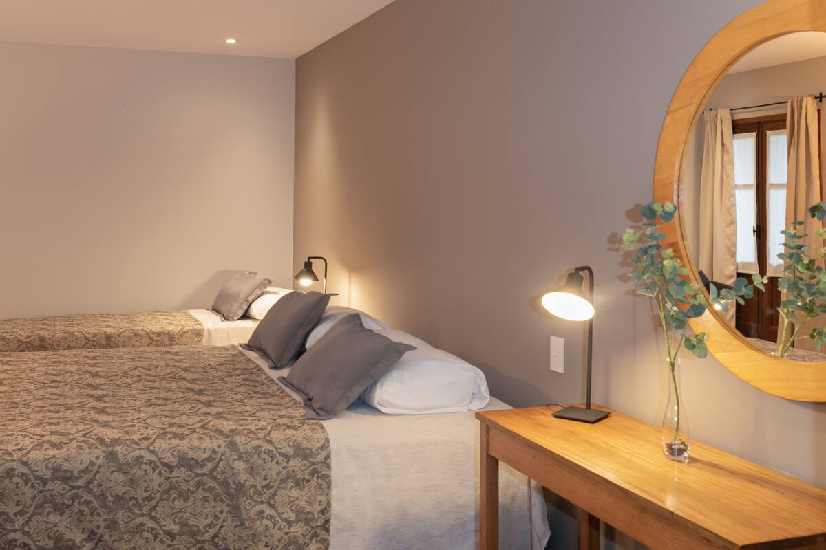 A neatly arranged bedroom with a large bed, bedside tables, a mirror, and a vase with flowers.