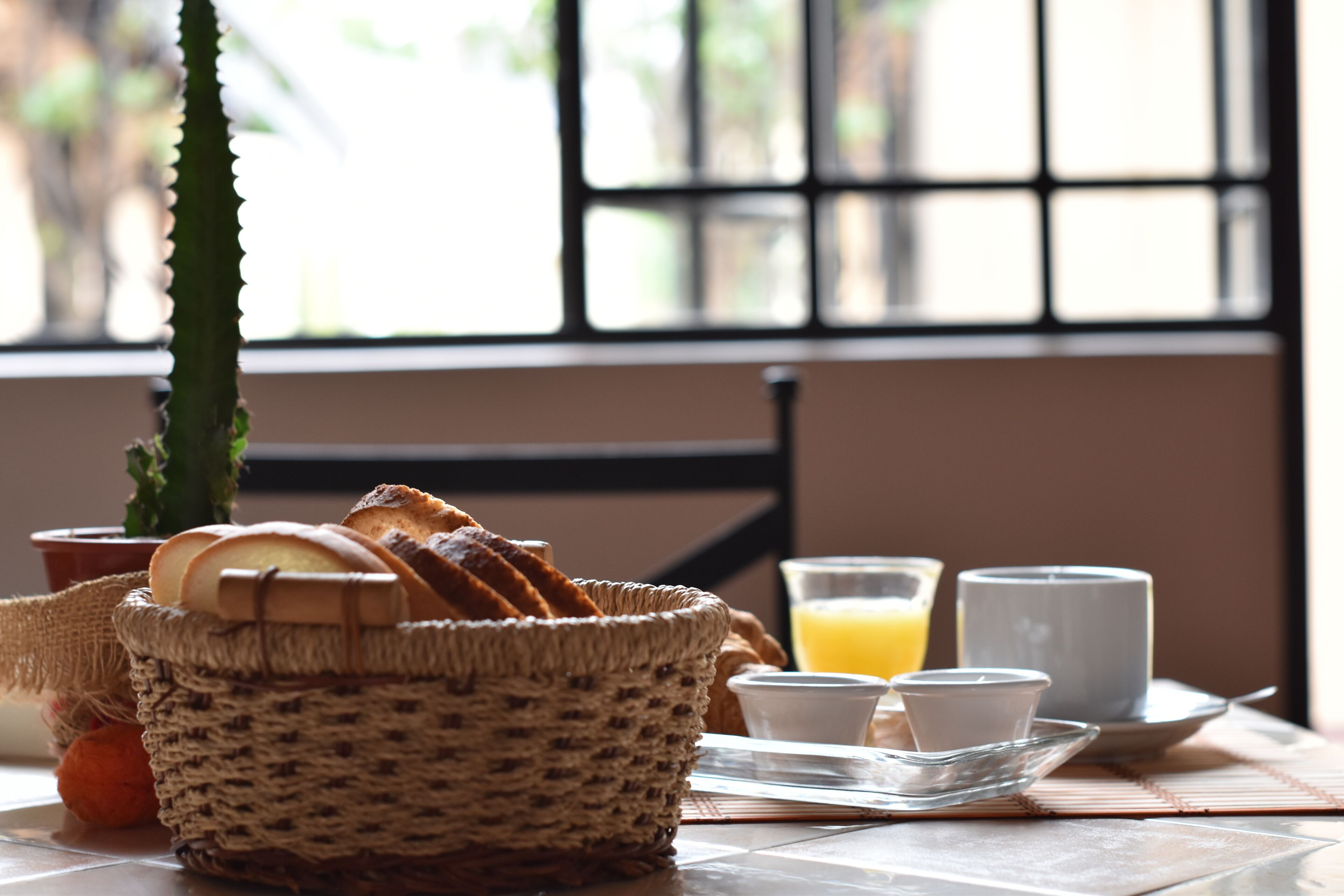 A breakfast setting with bread, a cactus, and a table with a glass of orange juice and a cup.