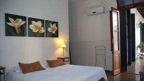 Hotellihuone, jossa on sänky, yöpöytä, lamppu ja kolme seinälle ripustettua kukka-aiheista taulua.