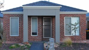 A two-story house with a brick facade, a front porch, and a metal gate. - The New Waves (POINT COOK)