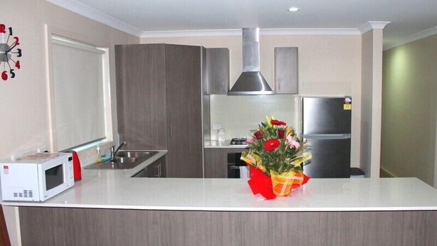 A modern kitchen with a white countertop, stainless steel appliances, and a decorative flower arrangement. - The New Waves (POINT COOK)