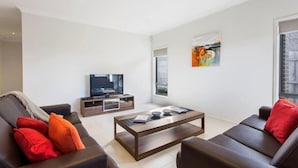 A modern living room with a sofa, coffee table, TV, and artwork on the wall. - Bradford Place (GLADSTONE PARK)
