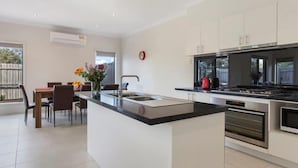 A modern kitchen with a central island, stainless steel appliances, and a dining area with a table and chairs. - Bradford Place (GLADSTONE PARK)