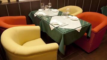 A dining area with a table set for two, featuring a green tablecloth and two chairs, one yellow and one orange.