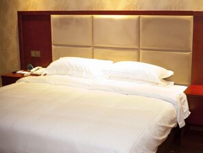 Een hotelkamer met een groot bed, een houten hoofdbord en een nachtkastje met een telefoon en een glas water.