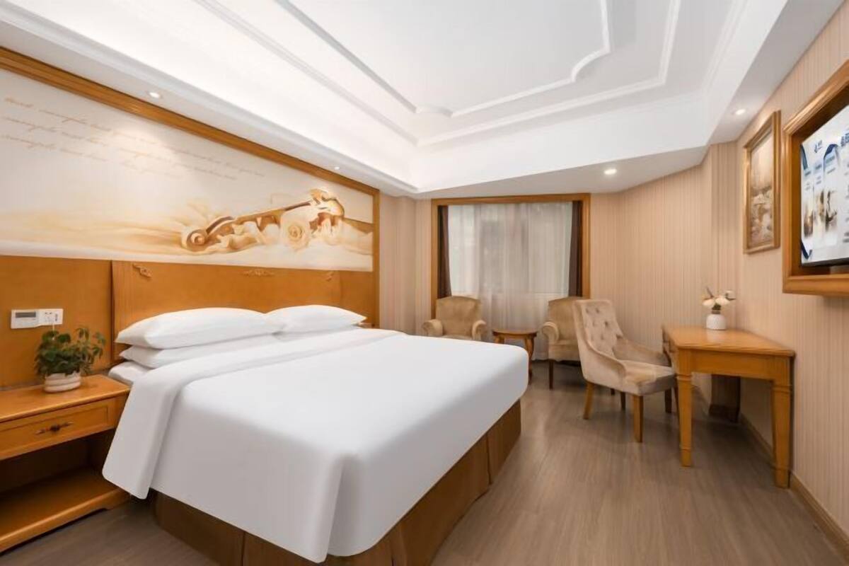 A hotel room with a large bed, a desk, a chair, and a small table.