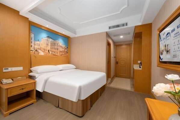 A hotel room with a bed, a nightstand, a wall-mounted TV, and a poster.