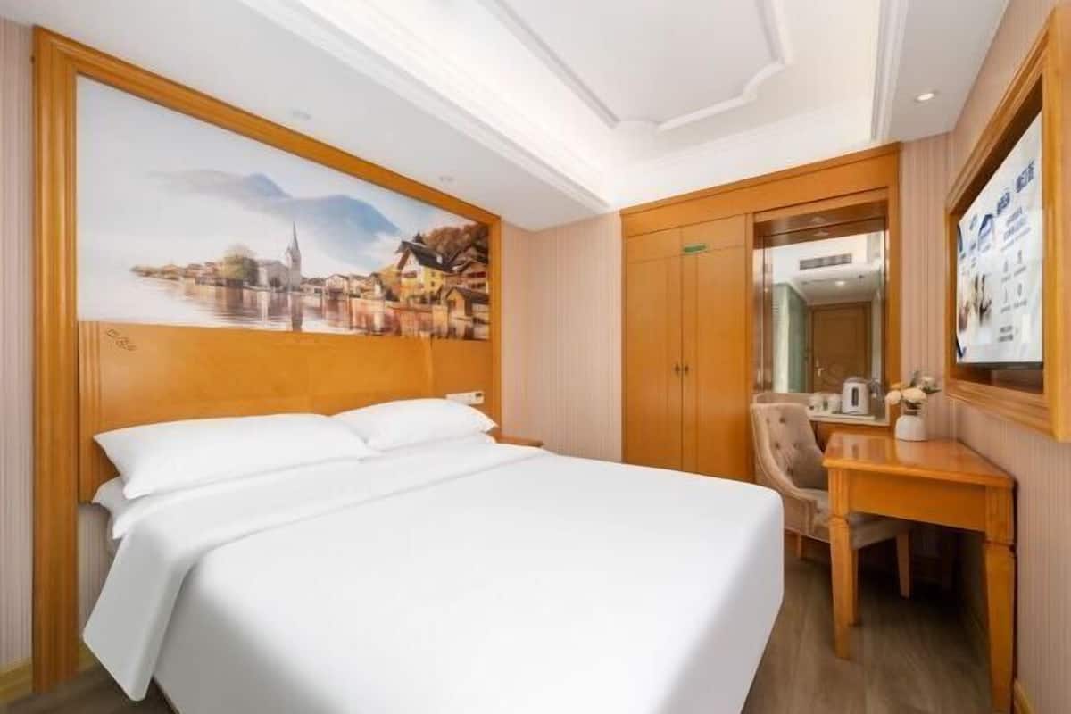 A hotel room with a large bed, a desk, a chair, and a painting on the wall.