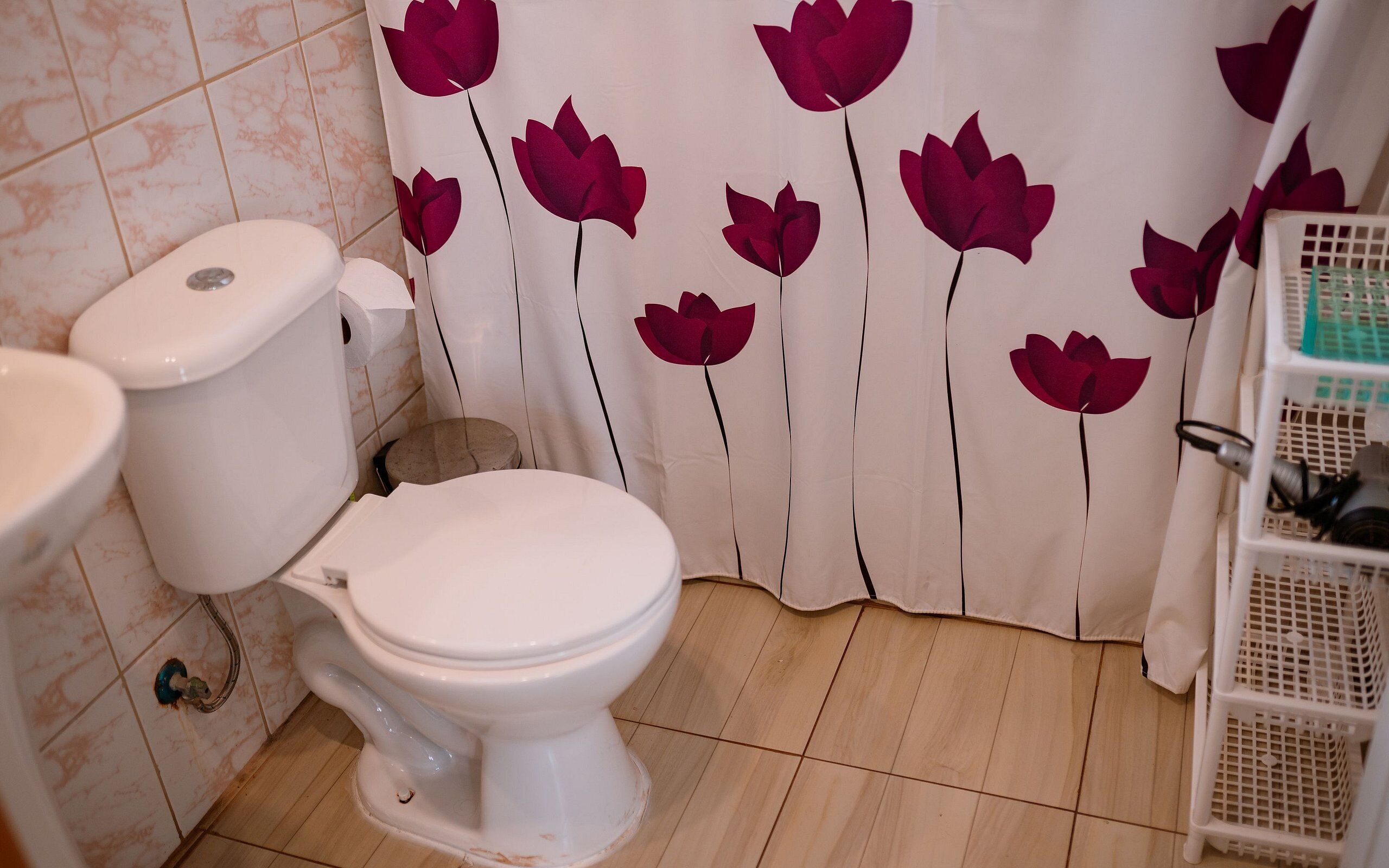 Un baño con inodoro, lavamanos y cortina de ducha estampada con flores.