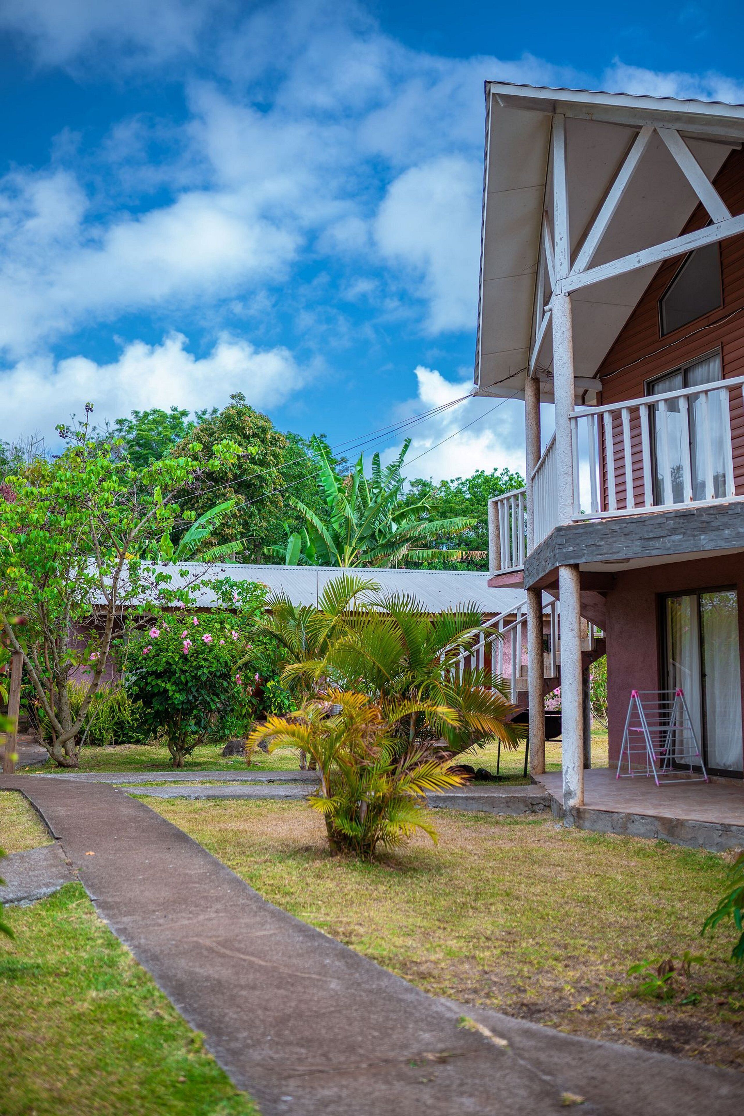 A bungalow with a balcony, surrounded by tropical vegetation and a clear sky.