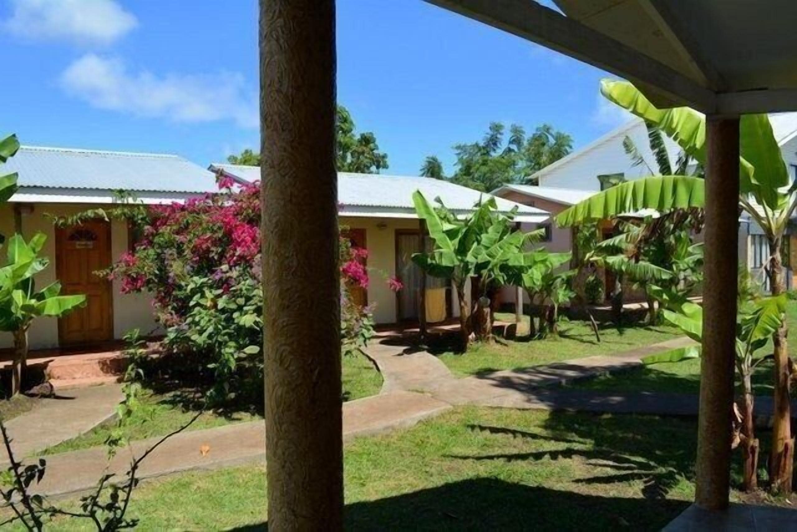 A bungalow with a covered porch, a garden with tropical plants, and a clear blue sky.
