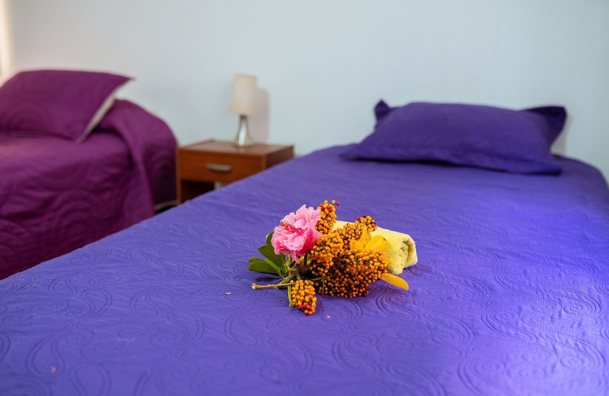 A bed with a purple bedspread and a bouquet of flowers on it.