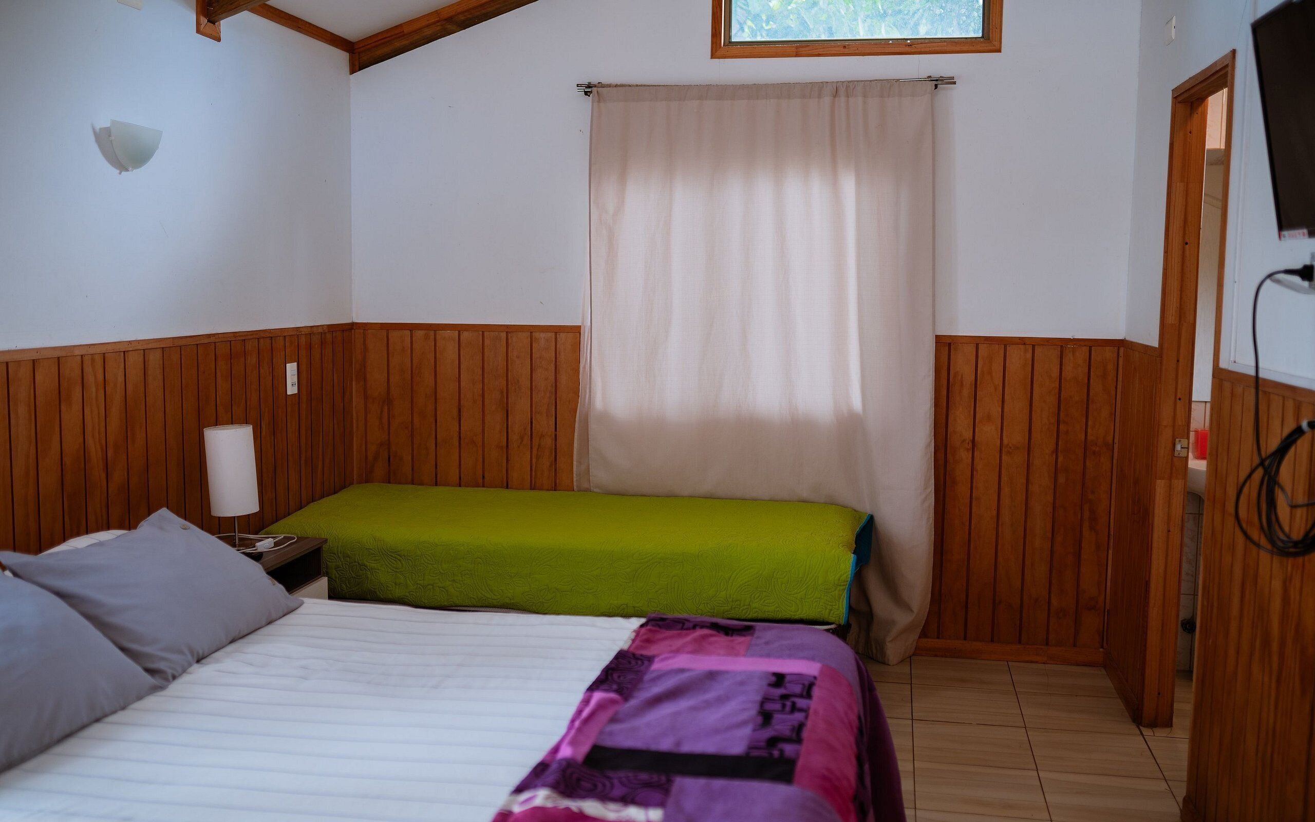 A room with two beds, wooden paneling, a window with a curtain, and a television.