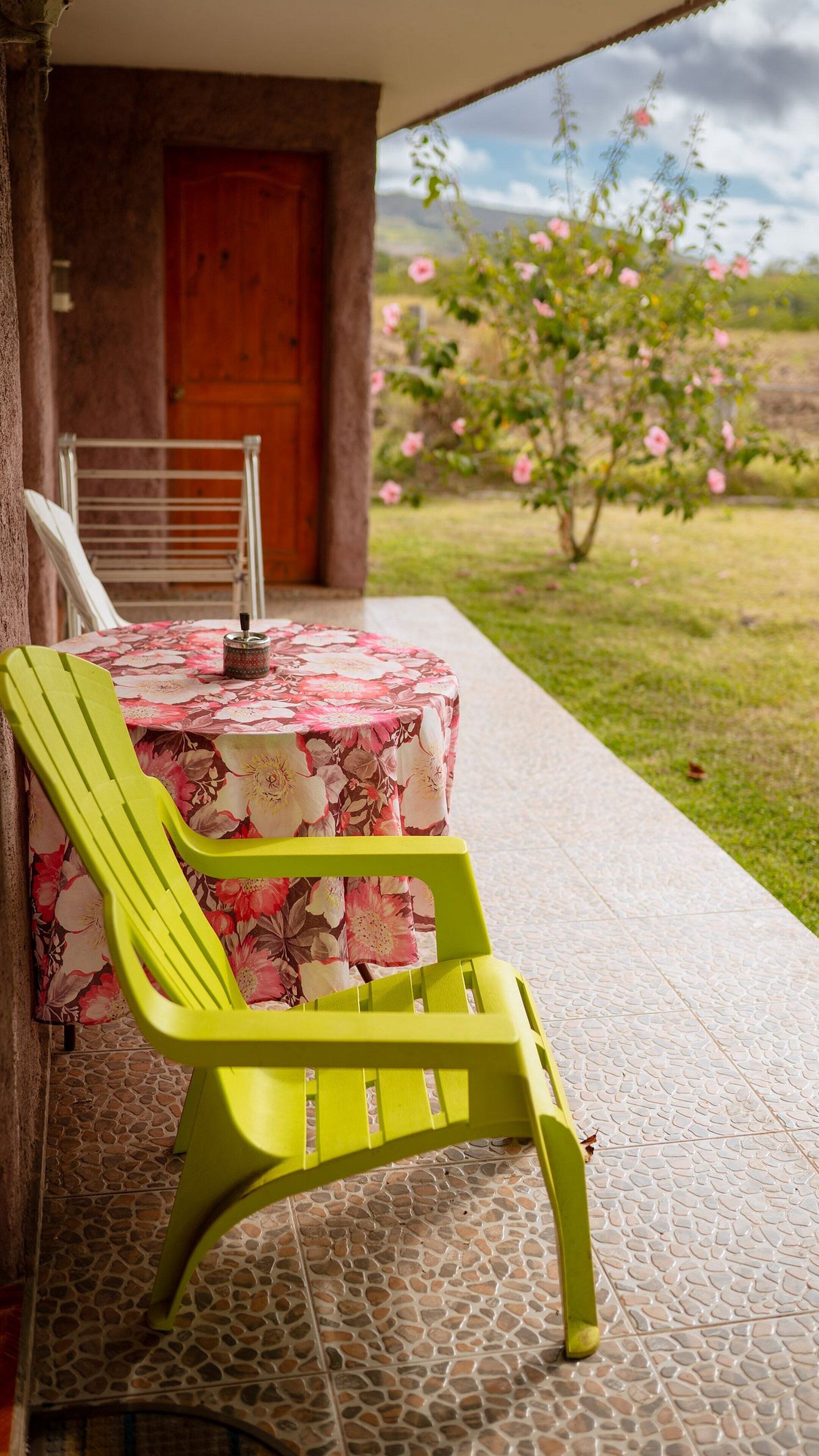 A patio with a table covered in a floral tablecloth, a bright green chair, and a stone-tiled floor.