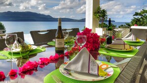 A table set for dining with a bottle of wine, glasses, and a view of the sea and mountains. - Villa Salamandra (Las Galeras)