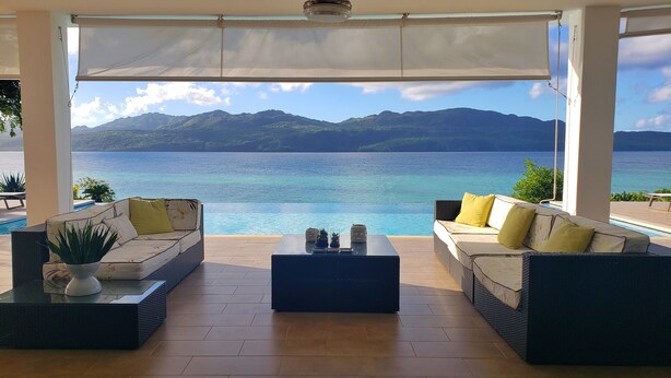 A covered outdoor seating area with two sofas facing a pool and a view of the sea and mountains. - Villa Salamandra (Las Galeras)