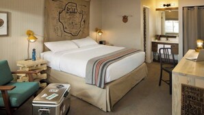 Une chambre d’hôtel avec un lit, un bureau avec un ordinateur portable, une chaise, une valise et une carte géographique accrochée au mur.