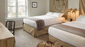 Une chambre d’hôtel avec deux lits, un bureau et une chaise. Il y a une fenêtre avec des rideaux, une carte accrochée au mur et une lampe sur la table de chevet.
