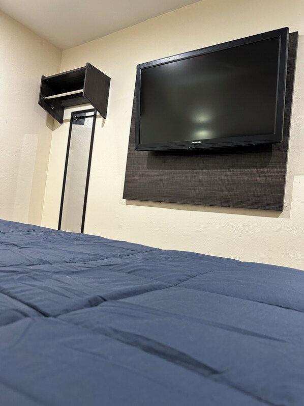 Ein Schlafzimmer mit einem Bett, einem an der Wand befestigten Fernseher und einem Lautsprecher auf einem Ständer.