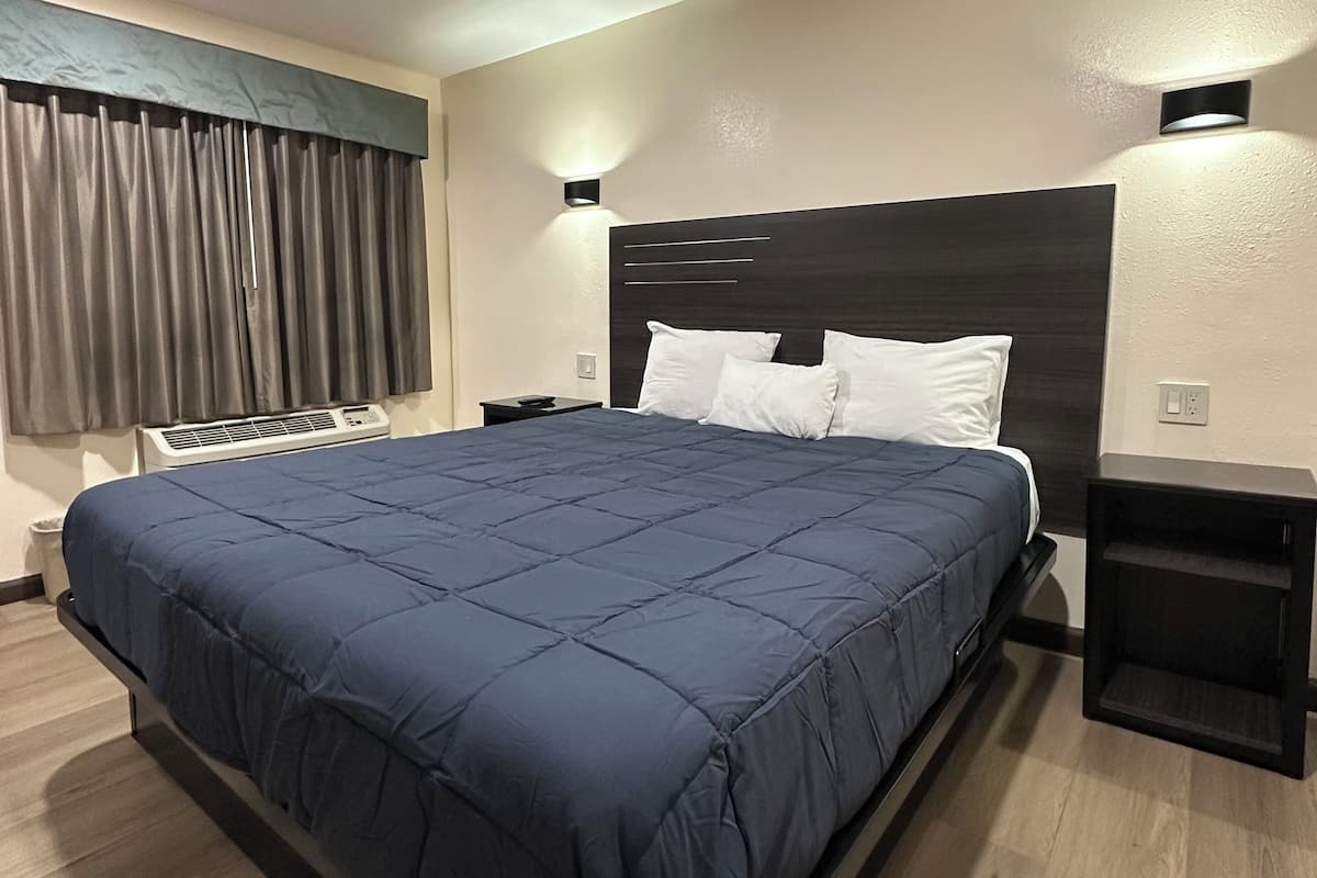 A modern hotel room with a large bed, dark headboard, and bedside tables.