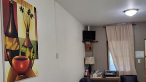 Une pièce avec un tableau représentant des vases, un bureau avec un ordinateur, une chaise et un lit avec des serviettes.
