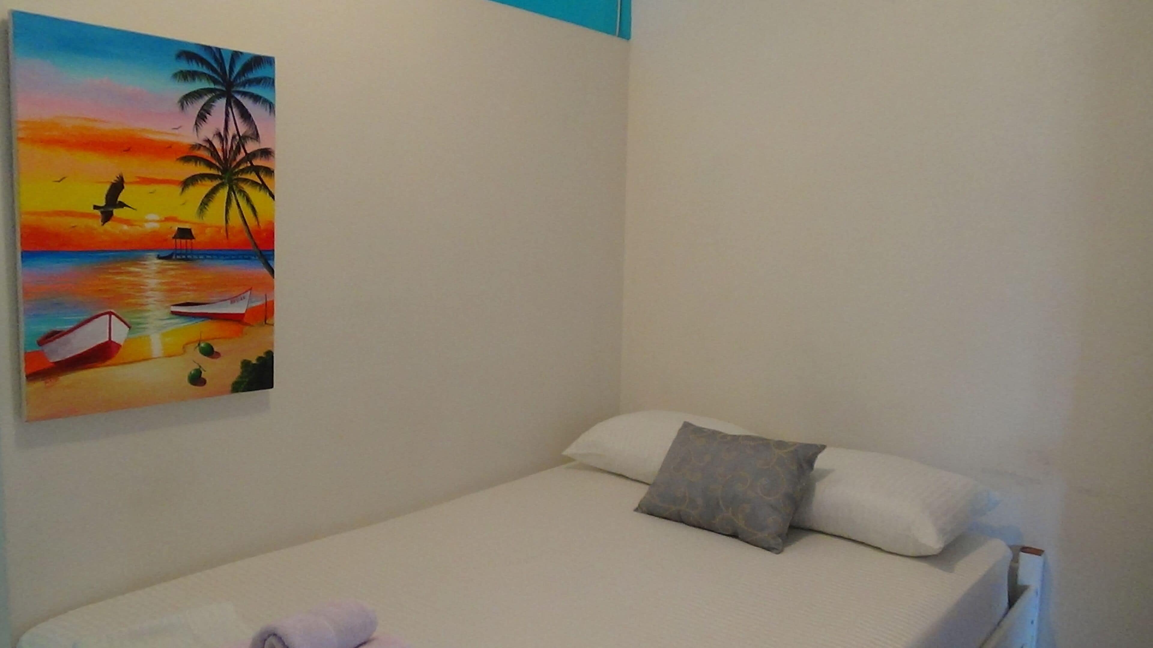 Uma cama de solteiro com travesseiro e um quadro de uma paisagem de praia na parede.