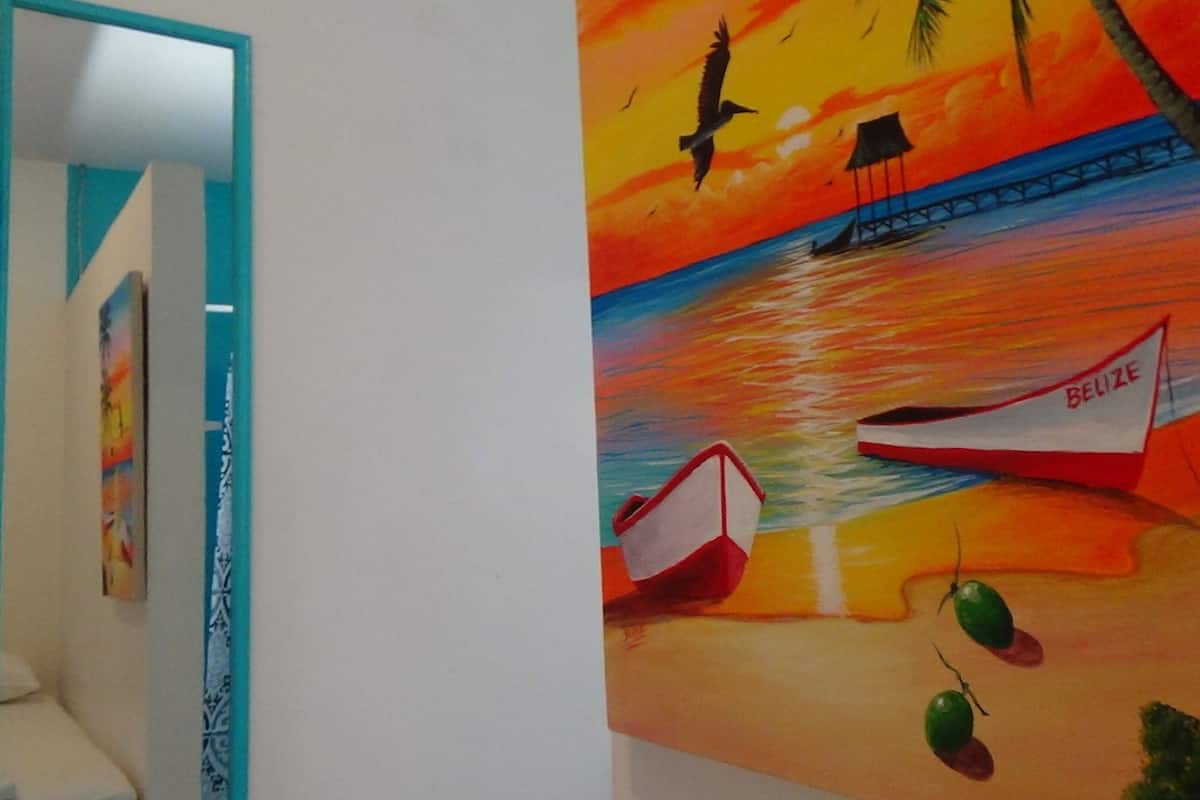 Un couloir orné d’un tableau représentant un bateau sur une plage, un pont et un oiseau dans le ciel.