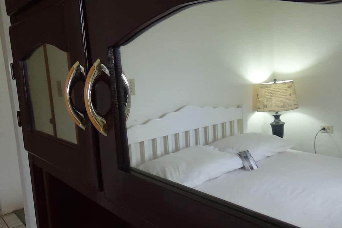 Une chambre à coucher avec un cadre de lit en bois, une tête de lit blanche, une lampe de chevet et un miroir.