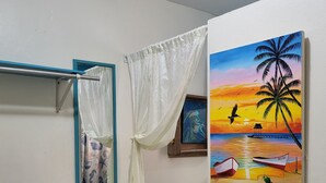 Une salle de bain avec un rideau de douche, un ventilateur fixé au mur et un tableau représentant une scène de plage.