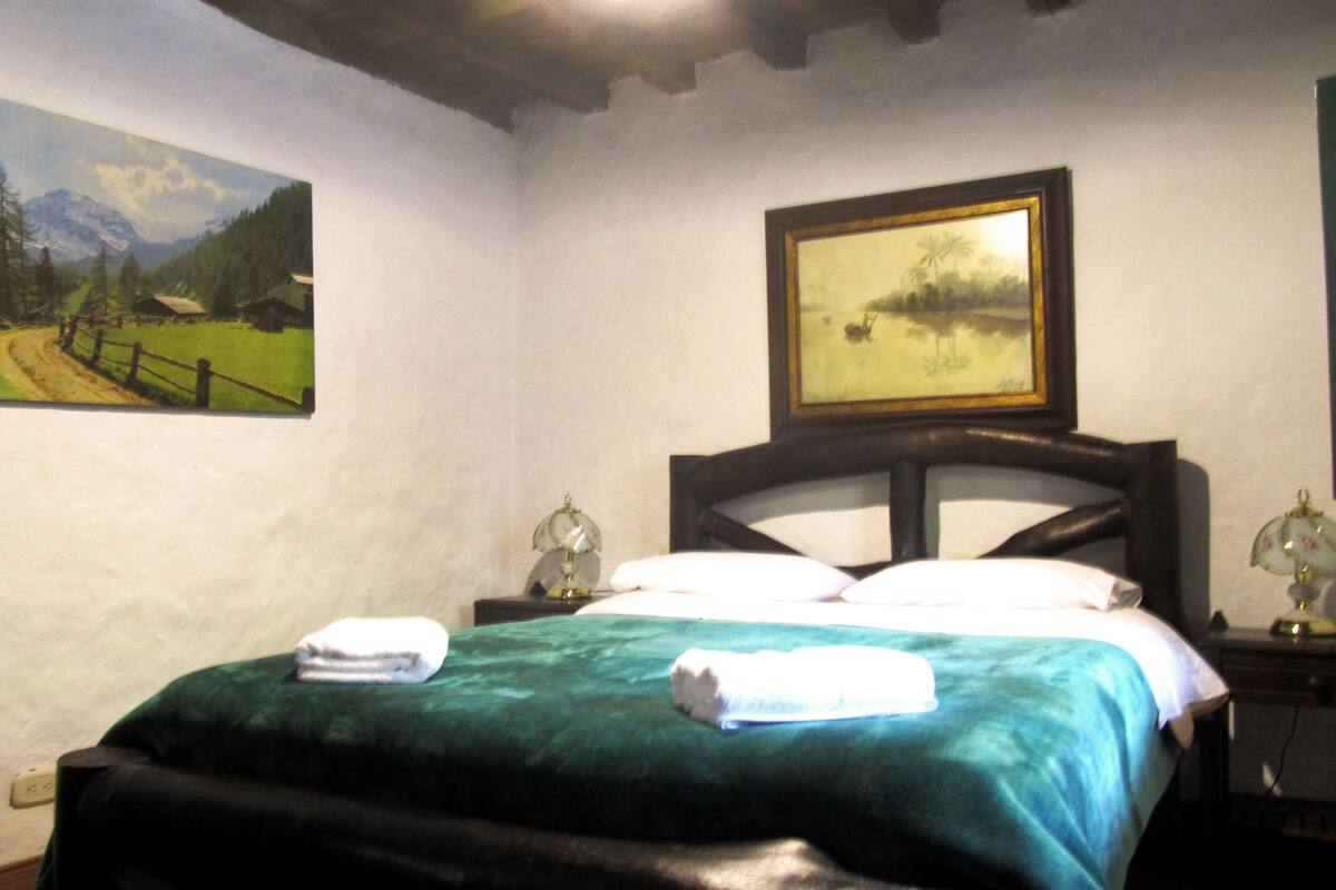 A bedroom with a bed, two bedside tables, a painting on the wall, and a window.