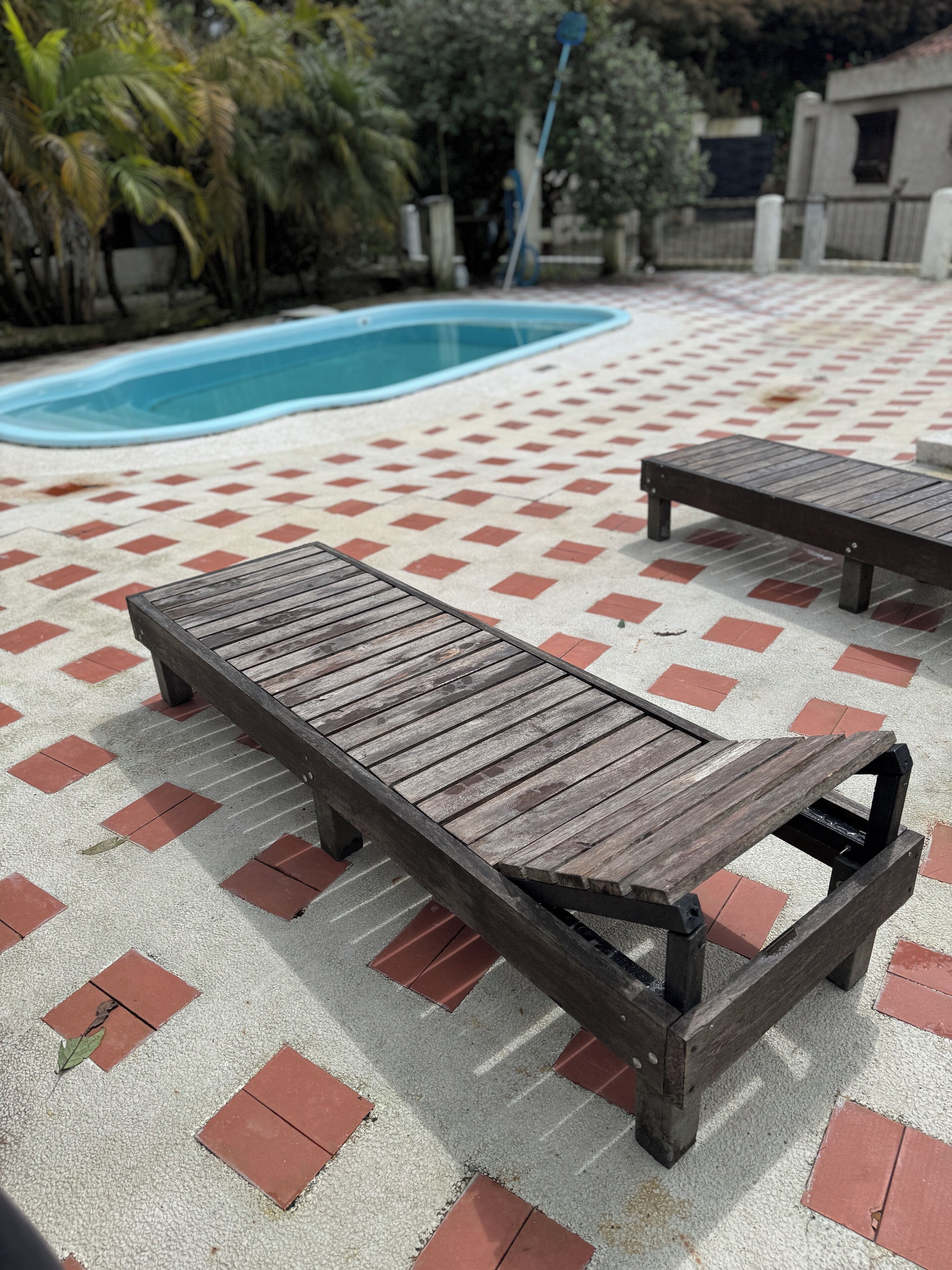 Zona de piscina con suelo de baldosas y dos sillones de madera.