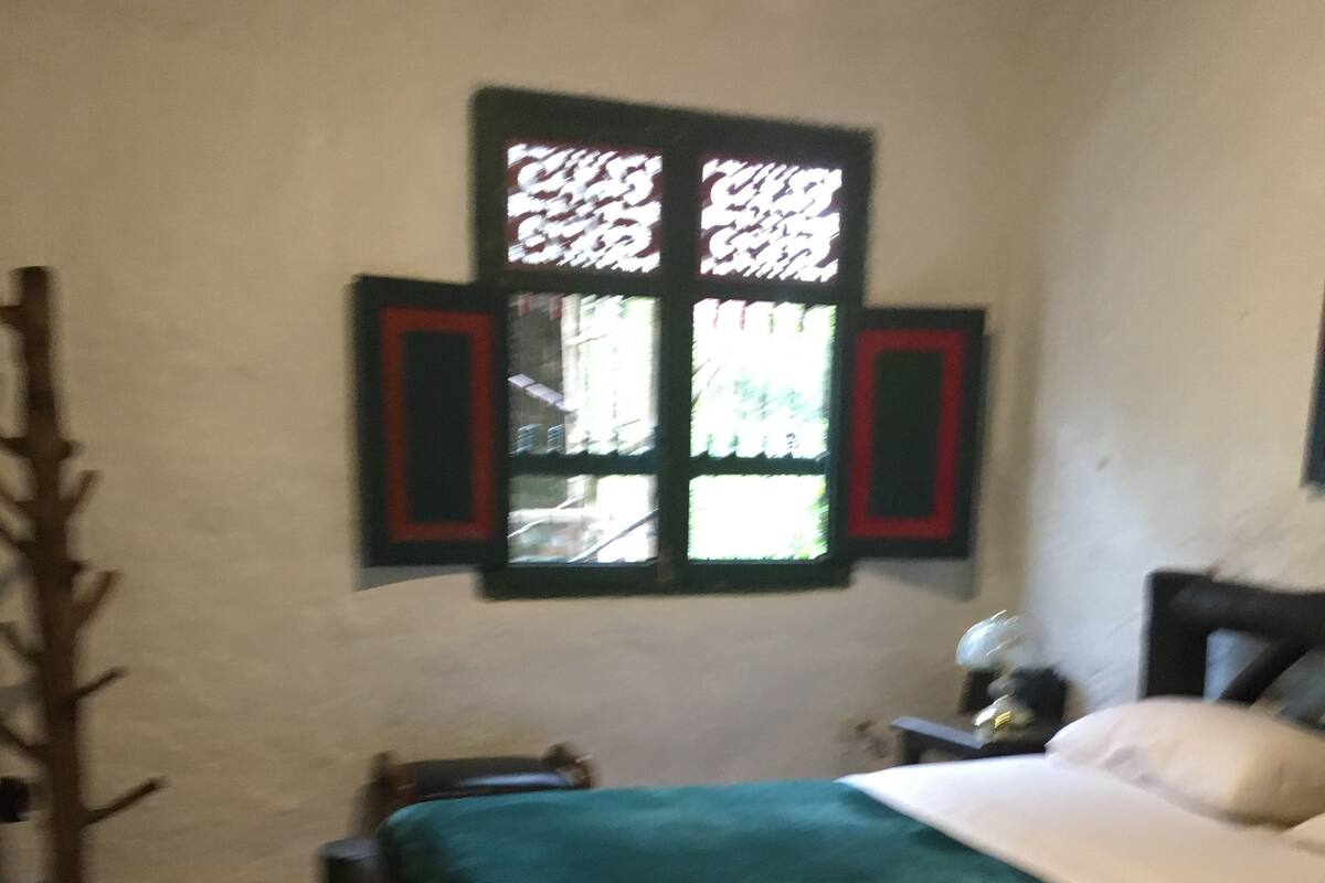 A bedroom with a bed, a nightstand, a lamp, and a window with shutters.